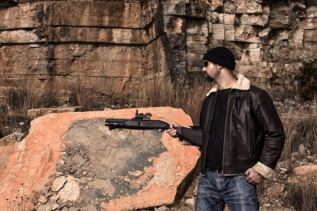 View of a man with a shotgun in jeans and jacket on a stone quarry.の写真素材