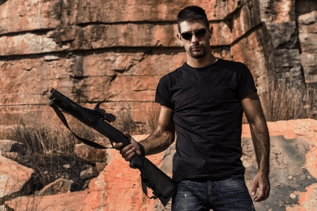 View of a man with a shotgun in jeans and black shirt on a stone quarry.の写真素材