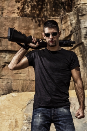 View of a man with a shotgun in jeans and black shirt on a stone quarry.の写真素材