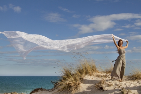 View of a beautiful girl in beach holding a beautiful long white cloth in the wind.の写真素材