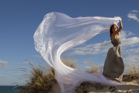 View of a beautiful girl in beach holding a beautiful long white cloth in the wind.の写真素材