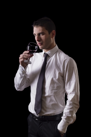 View of a young man holding a red glass of fine wine isolated on black studio background.の写真素材