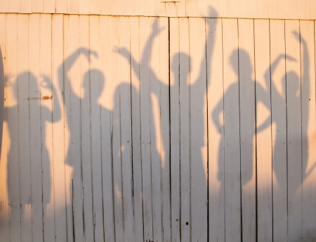 View of a fun photo of a group of friends making poses creating a shadow on a wooden wall.の写真素材