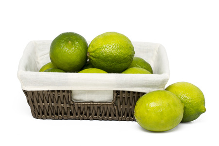 Close up view of a bunch of lime fruits inside a wicker basket isolated on a white background.の写真素材