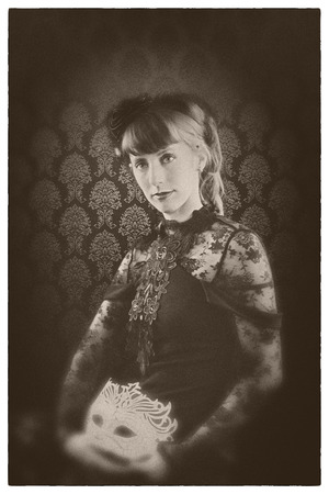 Beautiful girl on a black gothic dress with a white mask on a vintage sepia look.の写真素材