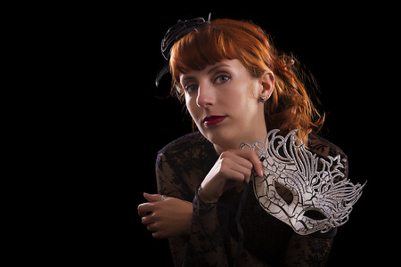 Beautiful girl on a black gothic dress with a white mask isolated on a black background.