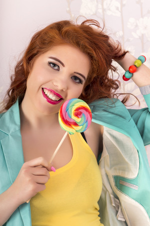 View of a beautiful redhead girl with a lollipop candy wearing colorful clothing.の写真素材