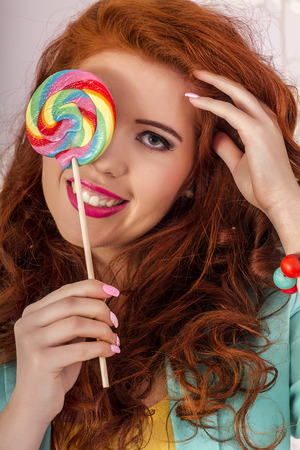 View of a beautiful redhead girl with a lollipop candy wearing colorful clothing.の写真素材