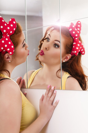 View of a beautiful redhead girl with colorful pinup clothes next to a mirror wall.の写真素材
