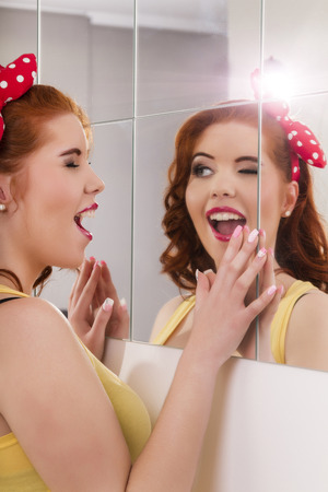View of a beautiful redhead girl with colorful pinup clothes next to a mirror wall.の写真素材