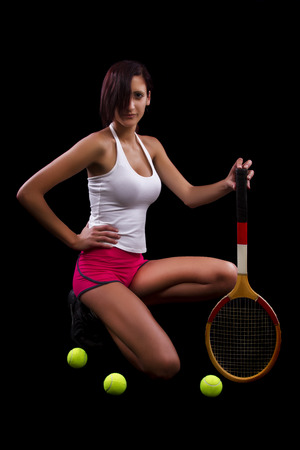 Beautiful young girl with a tennis racquet on a black background.の写真素材