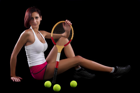 Beautiful young girl with a tennis racquet on a black background.の写真素材