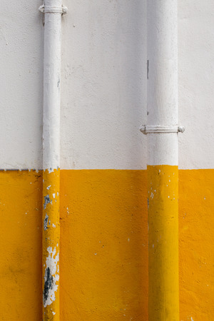 Close up view of a wall half painted in yellow and white with pipes.の写真素材