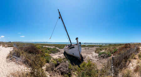 Abandoned boat on the vegetation on the sand dunes of Ria Formosa marshlands located in the Algarve, Portugal.の写真素材