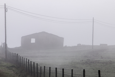 Foggy countryside with a wooden fence and a house.の写真素材