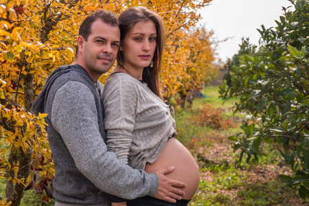 husband and pregnant wife in nature next to a yellow tree.の写真素材
