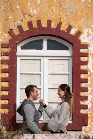 Husband with pregnant wife next to their old house.の写真素材