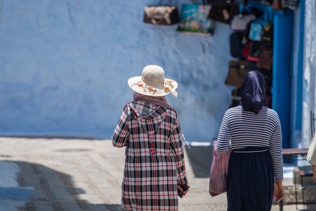 Women in typical moroccan clothing, walking down a street in Chefchaouen city.の写真素材
