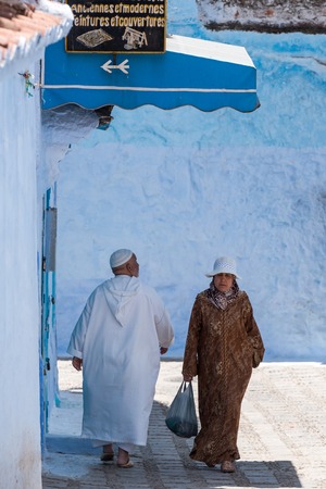 CHEFCHAOUEN, MOROCCO - JUNE 11, 2016: A couple pass by each other in typical moroccan clothing, in Chefchaouen city.のeditorial素材