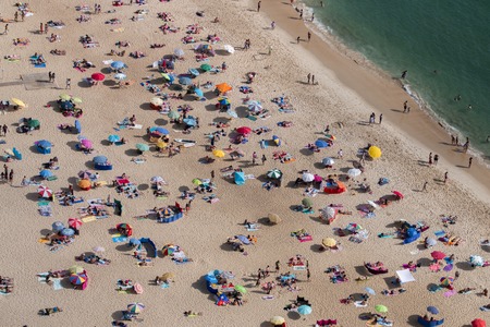 Crowded beach full of tourists in summer, located in Nazare city, Portugal.