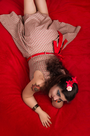 Pinup girl posing on red blacket bed in her bedroom.の写真素材