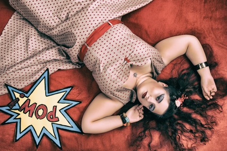 Pinup girl posing on red blacket bed in her bedroom.の写真素材