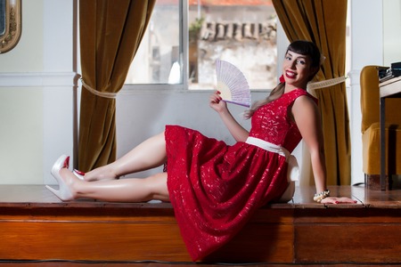 Pinup girl with red dress next to a classic window.の写真素材
