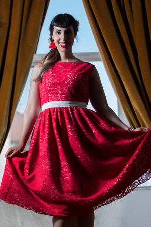 Pinup girl with red dress next to a classic window.の写真素材