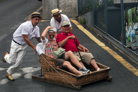 FUNCHAL, MADEIRA - 19th JUNE, 2017: Traditional toboggan men operating a wicker basket car with tourists.のeditorial素材