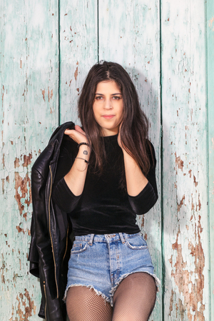 Close view of a beautiful young woman with short blue jeans over a green wooden background.のeditorial素材