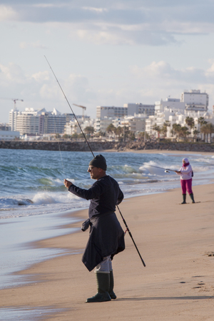 QUARTEIRA, PORTUGAL - 4th of February, 2018 - People fishing with a fishing rod from the shore in the beach to the sea.のeditorial素材