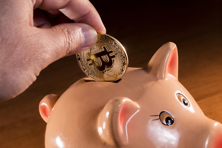 Male hand inserting bitcoin on porcelain piggy bank.の写真素材