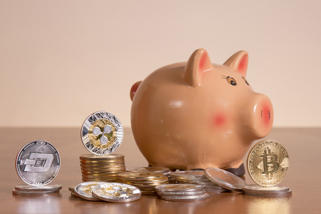 Piggy bank with several crypto currency coins on top of wooden table.の写真素材