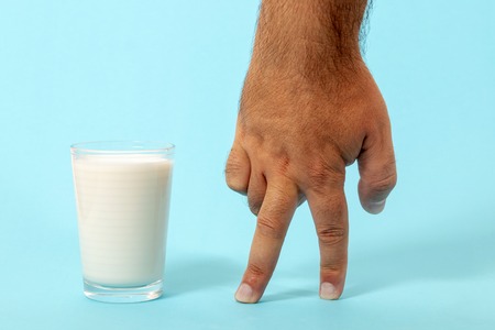 finger walking to glass of milk on a blue background.の写真素材