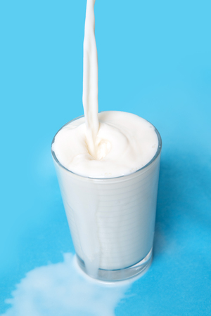 pouring milk on glass isolated on a blue background.の写真素材