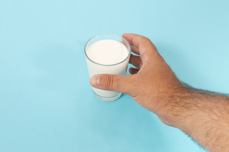 hand grabs glass of milk on a blue background.の写真素材