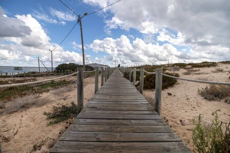 wooden path on the sand dunes shoreline on the beach of Faro region, Portugal.の写真素材