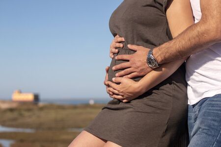 Hands of loving couple hold belly of pregnant woman.