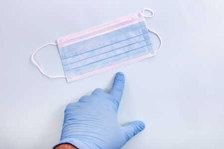 doctor hand in blue gloves pointing to face mask over a light blue background.