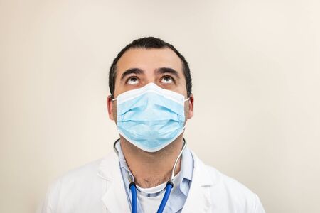 caucasian doctor with face mask portrait looking up on a white background.