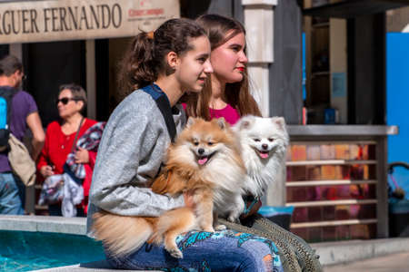 HUELVA, SPAIN - 22nd FEBRUARY 2020: Young female tourists with fluffy cute dogs near fountain.のeditorial素材