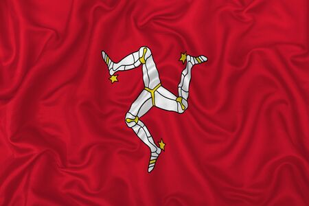 Isle of Man country flag on wavy silk textile fabric background.の写真素材