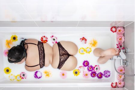 woman wearing sensual red lingerie on a milky bathtub with flowers.の写真素材