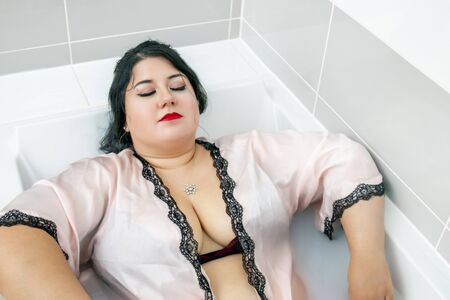 woman in sensual pink bathrobe and lingerie on a milky bathtub.の写真素材
