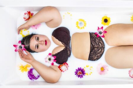 woman wearing sensual red lingerie on a milky bathtub with flowers.の写真素材