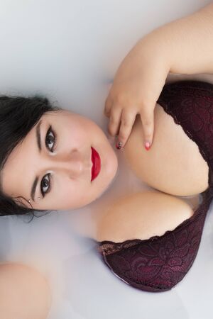 woman in sensual dark red lingerie on a milky bathtub.の写真素材