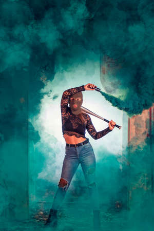 Dangerous girl with bat and balaclava on a abandoned factory using a smoke grenade.