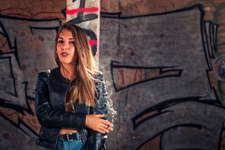 Model with leather jacket and blue jeans on a abandoned factory on sensual poses, smoking a cigar.の写真素材