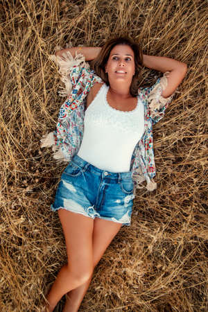 Beautiful girl posing on the countryside with short jeans on the dry grass vegetation.