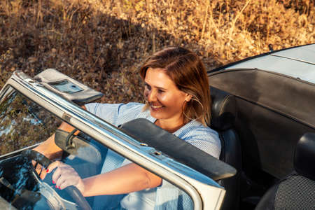 Woman with white convertible vintage car driving on the countryside.